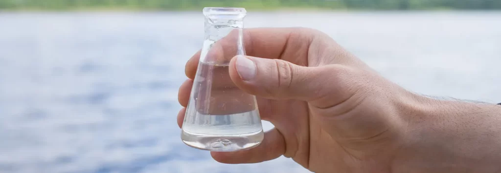 Water Purity Test. Hand holding a chemical flask with water, lake or river in the background.