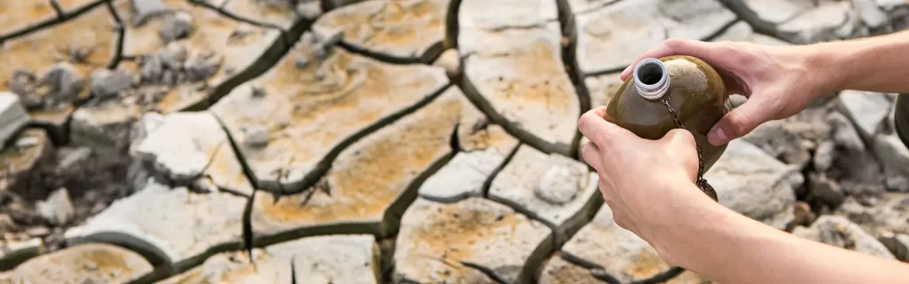 Hands holding a water canteen on a patch of cracked desert surface