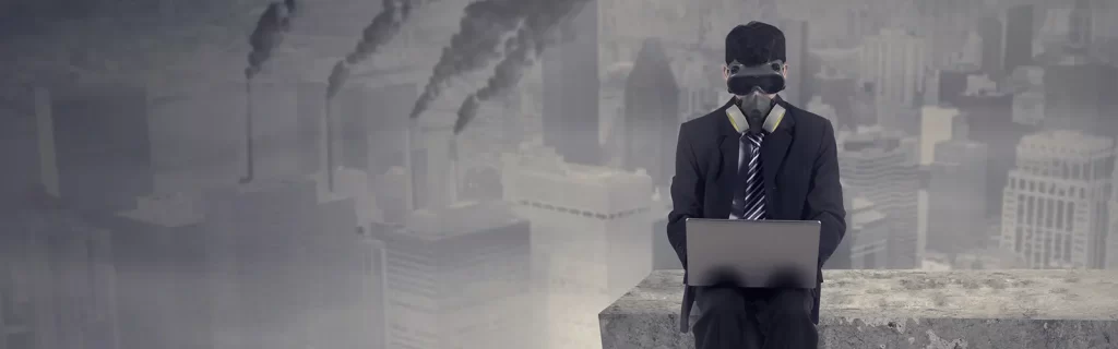 A man in a suit working on a computer with smoke stacks in the background