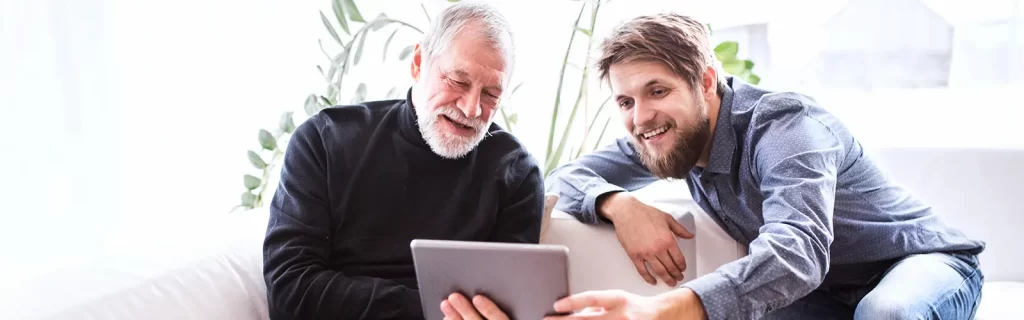 An old man using a tablet with a younger man